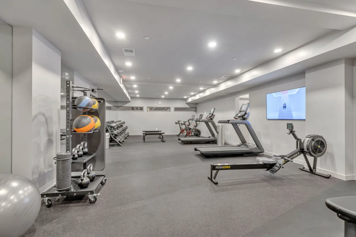 This image features a modern, well-equipped gym with treadmills, stationary bikes, a rowing machine, weight racks, and exercise balls. The room is brightly lit and spacious, creating an inviting environment to achieve fitness goals.