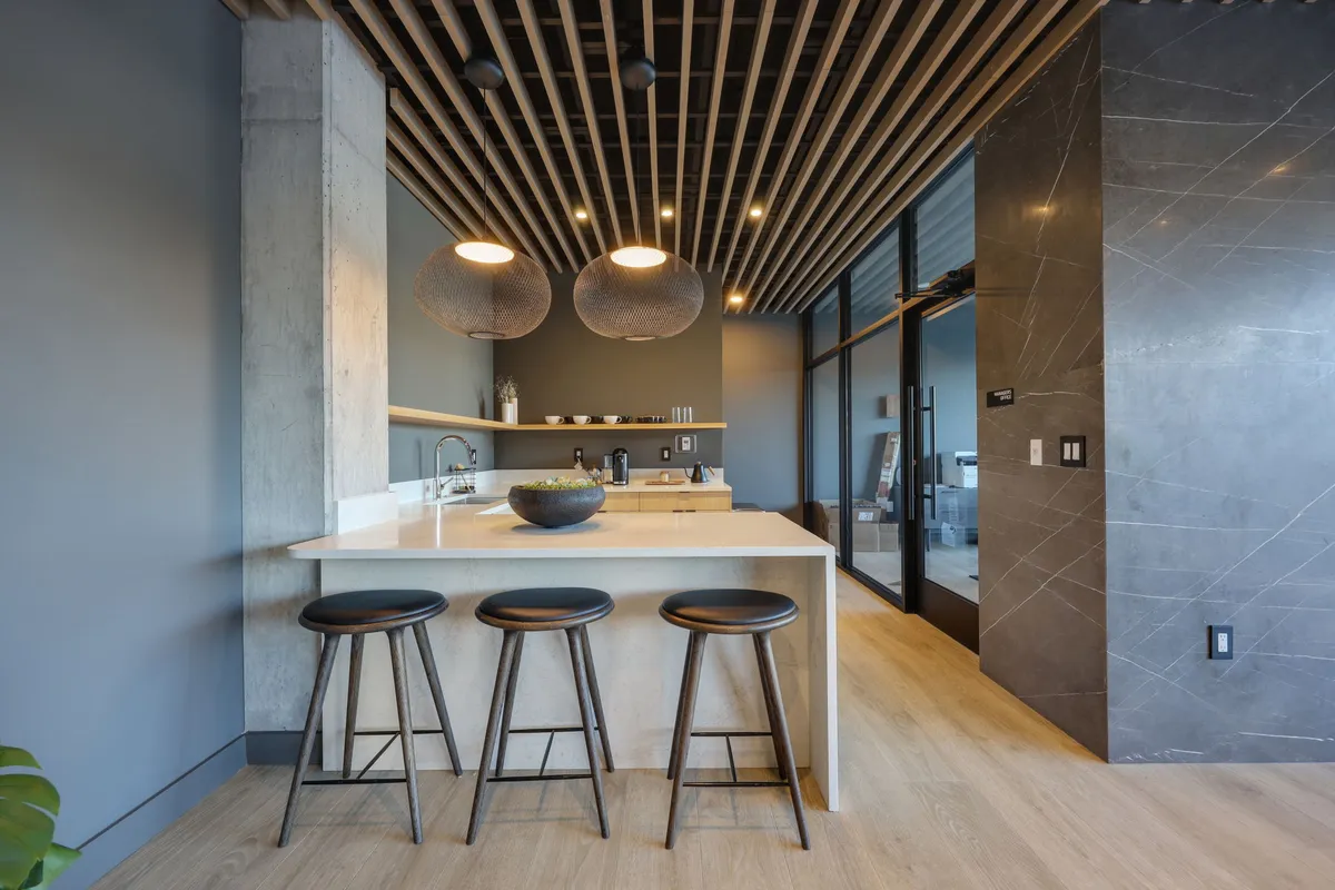 A contemporary kitchen with a central island, pendant lighting, bar stools, and a prominent concrete pillar. The kitchen is open to the rest of the space and designed for both cooking and socializing, making it ideal for entertaining or casual dining.