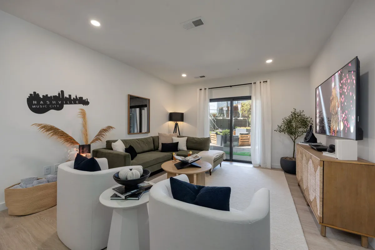 A cozy living area featuring a plush sofa, TV, coffee table, Nashville skyline art, and an indoor plant. The space feels comfortable and stylish, inviting relaxation or socializing, and is clearly professionally maintained.