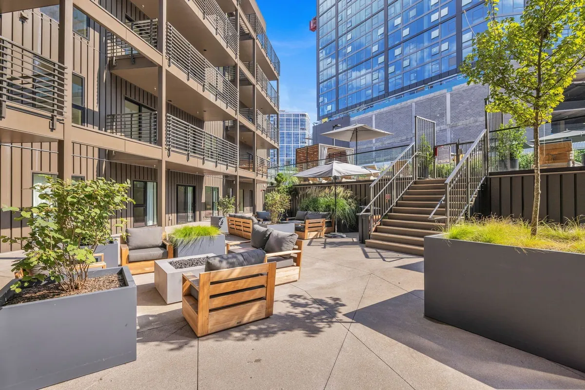 An outdoor seating area with modern architecture and lush landscaping, designed for social gatherings and relaxation. The space is set up for group conversations, outdoor dining, or simply enjoying time under the sky, both during the day and in the evenings.