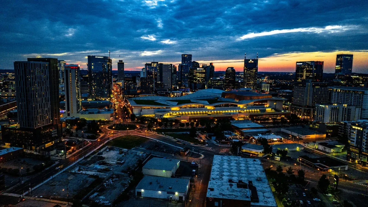 A panoramic view of the Nashville city skyline at sunset, with illuminated buildings, highways, and an energetic urban atmosphere. The image captures the dynamic cultural scene and easy access to city attractions.