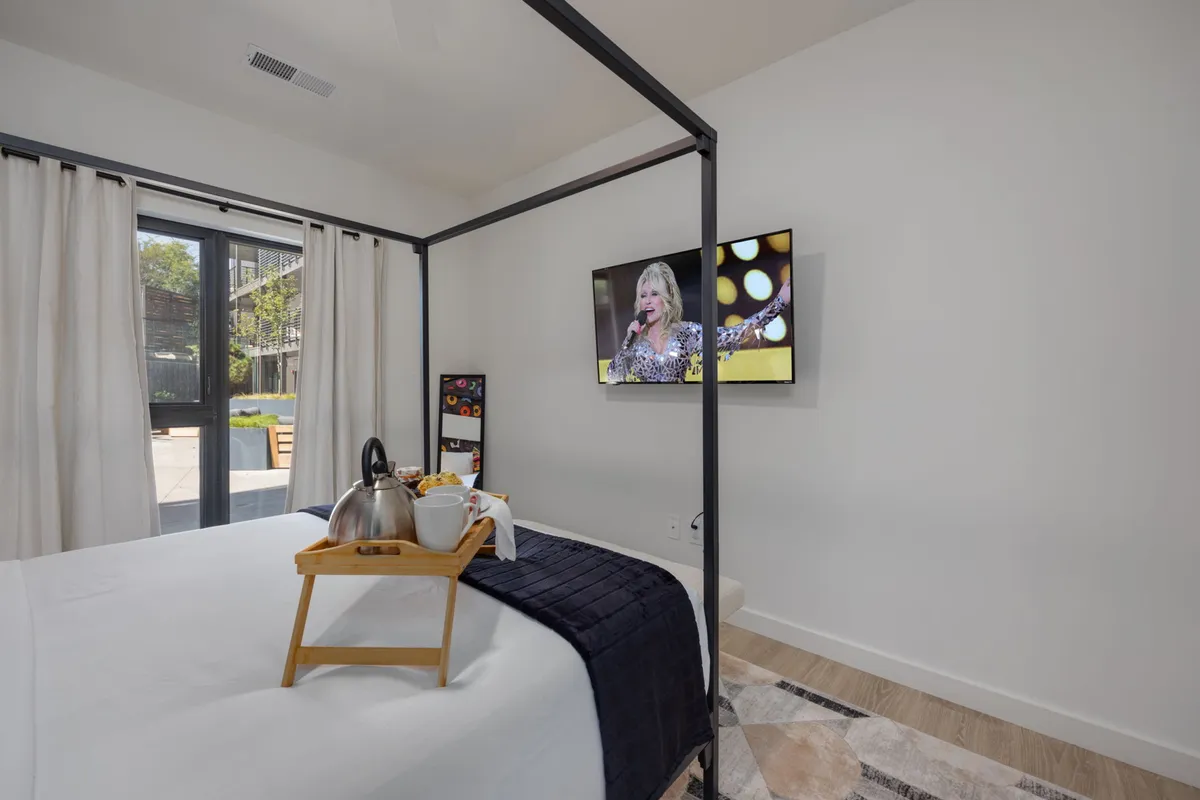 A tranquil bedroom scene with a grand four-poster bed, television screen mounted opposite, and a breakfast tray for leisurely mornings. The overall mood is peaceful and leisurely, providing a clear sense of privacy and modern comfort.