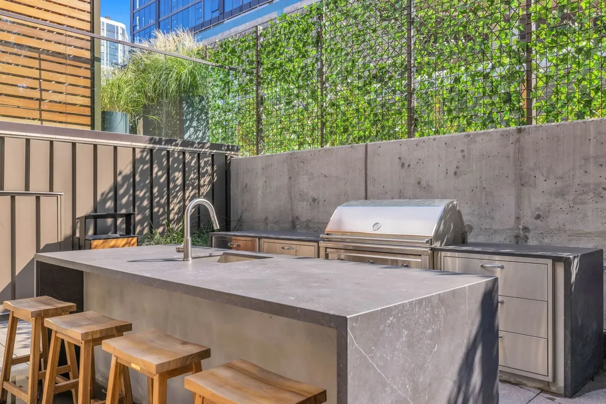 A contemporary outdoor kitchen island featuring a grill, bar stools, and an eye-catching green wall. The setup is designed for outdoor cooking and entertaining, ideal for casual barbecues or celebratory gatherings with friends.