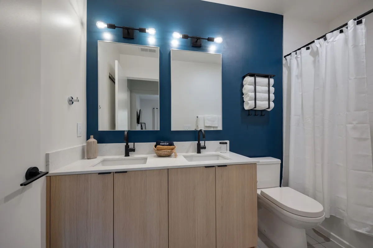A spacious en-suite bathroom with double sinks, large mirrors, and a soothing blue accent wall, designed for both morning routines and evening relaxation.